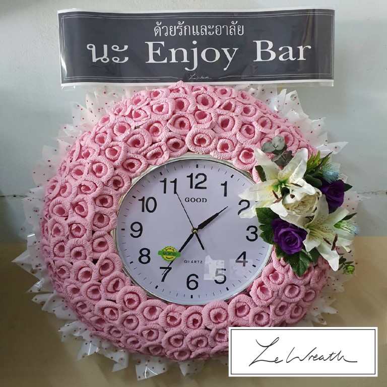 พวงหรีดนาฬิกา ตกแต่งด้วยดอกไม้จันทน์โทนสีชมพูอ่อน ตัดกับพื้นหลังสีขาวอย่างสวยงาม