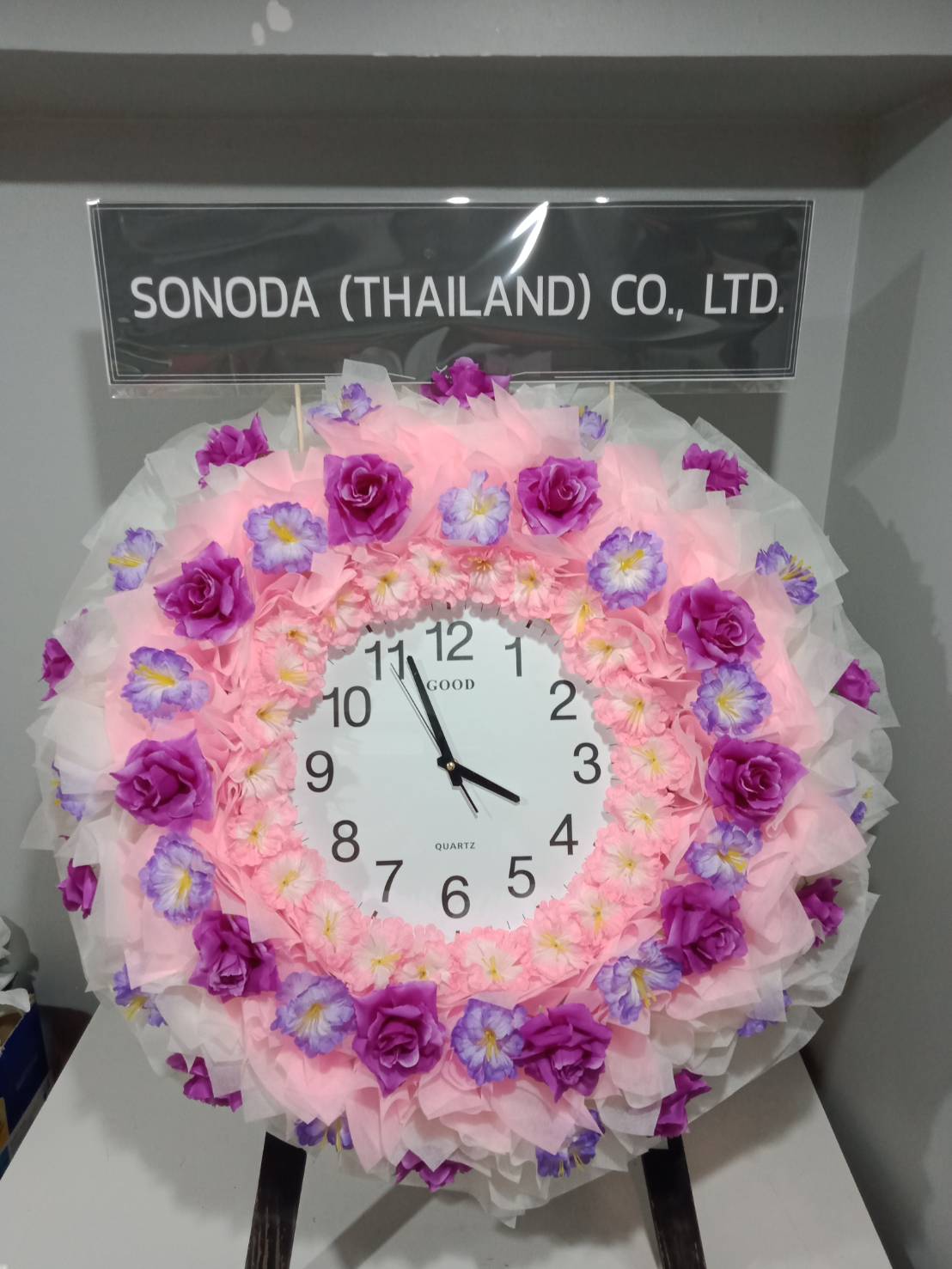 พวงหรีดนาฬิกากระดาษสา ชั้นนอกสีขาวและผ้าชั้นในสีชมพูแซมด้วยดอกไม้ประดิษฐ์สีม่วง